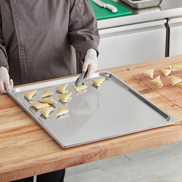 A person in a chef's uniform holding a Vollrath stainless steel steam table pan filled with food.