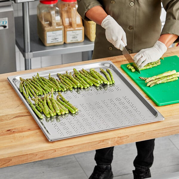 A person cutting asparagus on a Vollrath stainless steel tray on a counter.