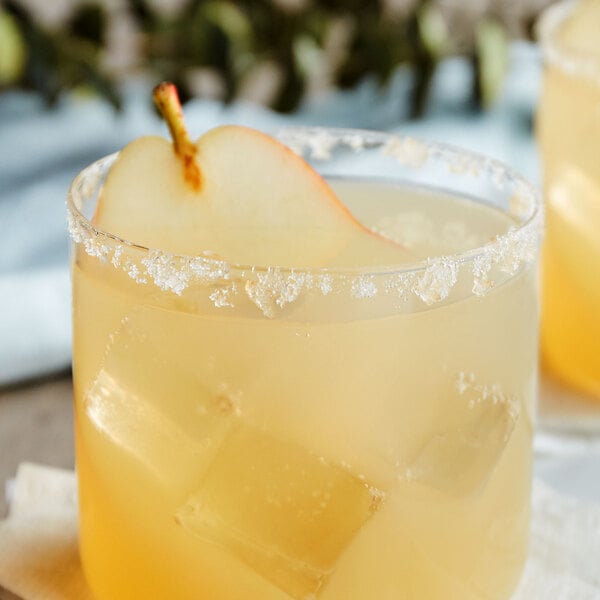 A glass of yellow liquid with a caramel vanilla pear garnish.