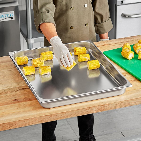 A person wearing gloves using a Vollrath stainless steel steam table pan to prepare corn on the cob.