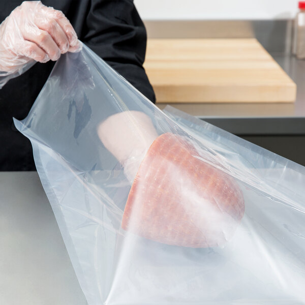 A person in a black glove holding a plastic bag of meat.