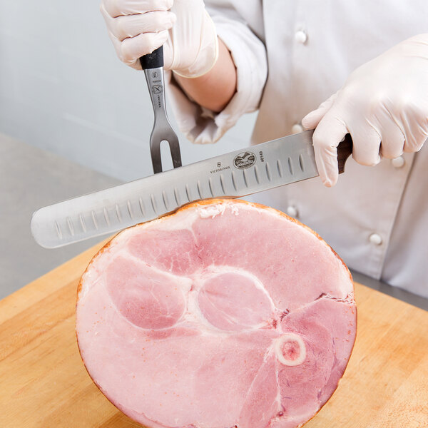 A person using a Victorinox carving knife to slice ham.