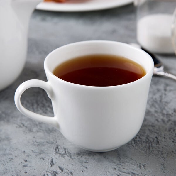 A close up of a white Reserve by Libbey bone china tea cup filled with tea on a table.