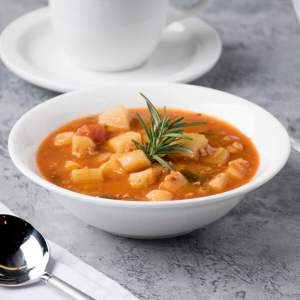 A close up of a white Reserve by Libbey bone china bowl containing soup with a sprig of rosemary.