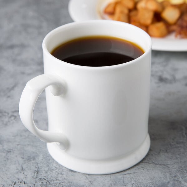 A white Reserve by Libbey bone china coffee mug with brown liquid on a plate.