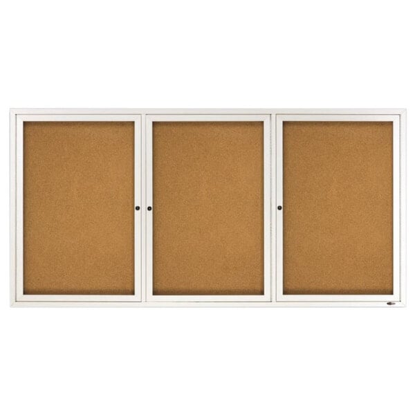 A silver aluminum enclosed bulletin board with a cork board inside and three white doors.