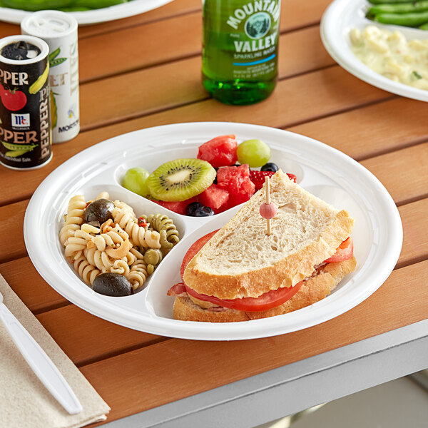 A white Dart Famous Service plastic plate with a sandwich, fruit, and a drink.