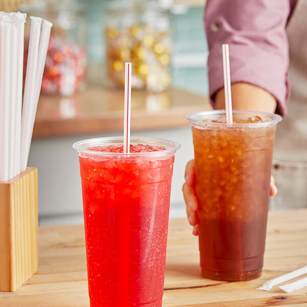 A person holding a cup of iced tea with a red and white striped straw.