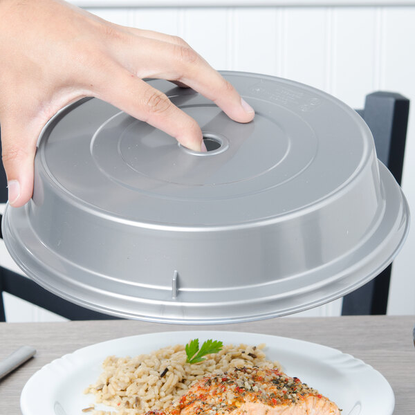 A hand holding a Cambro silver low profile plate cover over a plate of rice and meat.