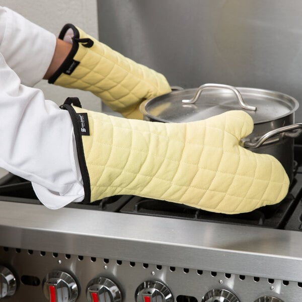 A person wearing yellow San Jamar oven gloves taking a pot off the stove.