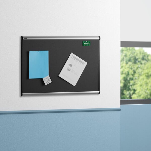 A blue wall with a Quartet Prestige bulletin board with black and white diamond mesh fabric.