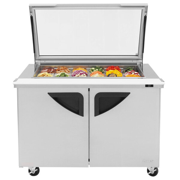 A Turbo Air stainless steel refrigerated sandwich prep table with glass lids over food trays.