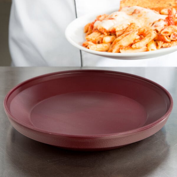 A person holding a Dinex insulated meal delivery base with a plate of pasta with cheese and sauce.