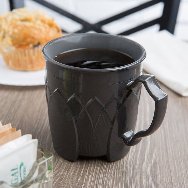 A cup of coffee sits on a table next to a muffin in a coffee shop.