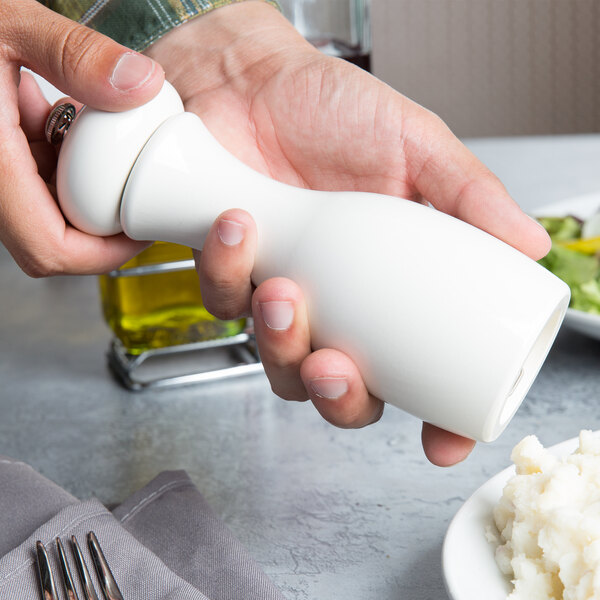 A person using a Fletchers' Mill white pepper grinder over a plate of food.