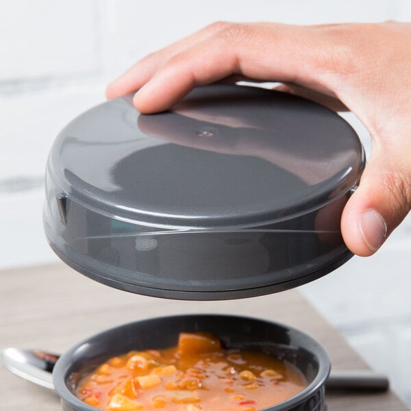 A person holding a grey Dinex soup bowl lid over a bowl of soup.