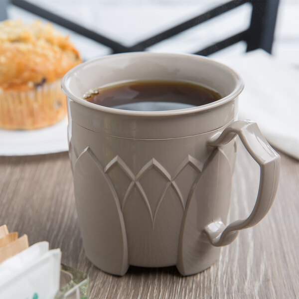 A Dinex Fenwick latte mug filled with coffee sits on a table next to muffins.