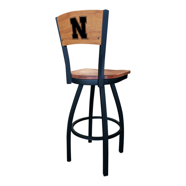 A bar height swivel chair with a black steel frame, maple back and seat, and a laser-engraved University of Nebraska 'N' logo on the backrest.
