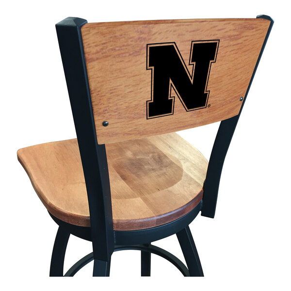 A wooden bar height swivel chair with a maple back and seat, featuring a black steel frame and a laser engraved University of Nebraska 'N' logo on the backrest.