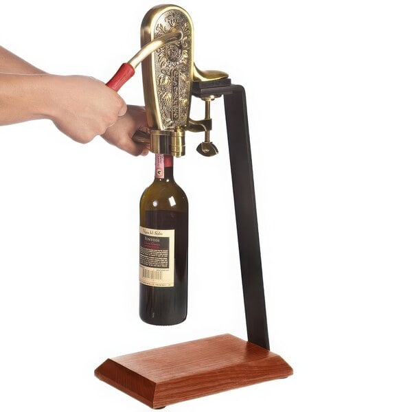 A person using a Franmara brass-plated wine bottle opener on a wooden counter stand.