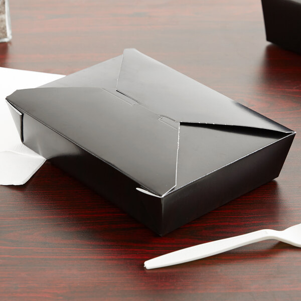 A black Fold-Pak Bio-Pak paper take-out box on a table with a white plastic fork and knife.