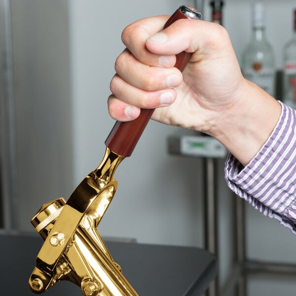 A hand using a Franmara brass-plated wine bottle opener with a brown and gold handle.