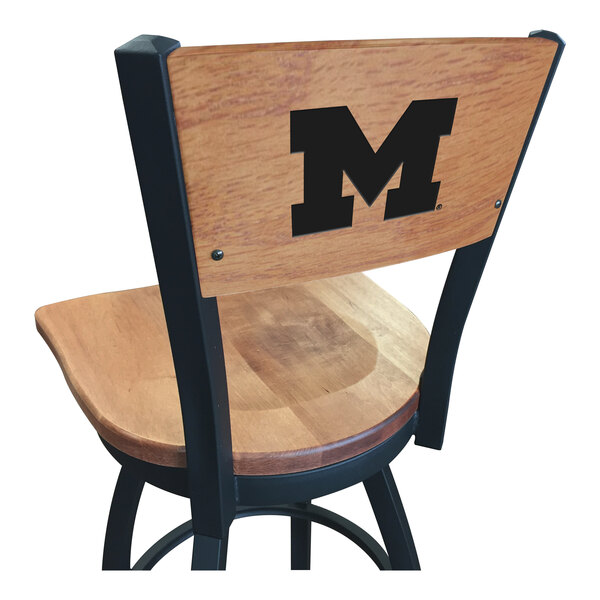 A black steel bar height chair with a maple wooden seat and back, with a University of Michigan logo on the back.