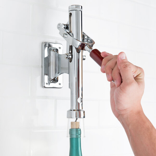 A hand using a Franmara wall mount wine bottle opener to open a blue bottle of wine.