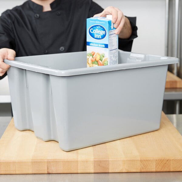 A person pouring a carton of milk into a Rubbermaid Palletote box on a counter.