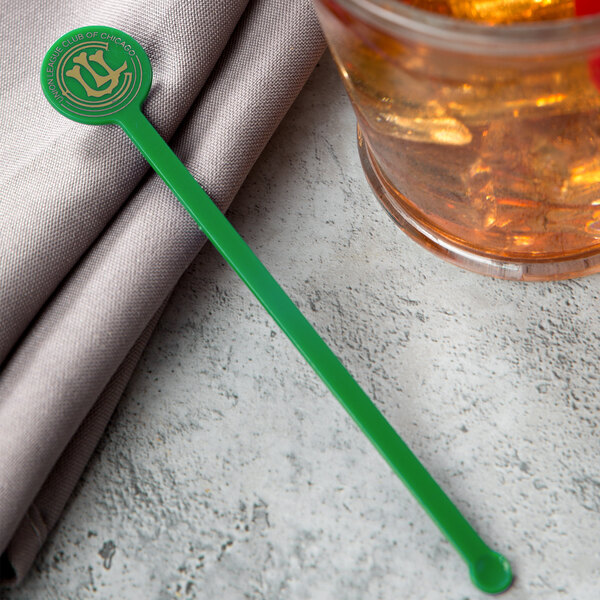 A glass of brown liquid with a green WNA Comet Spirit disc stirrer in it.
