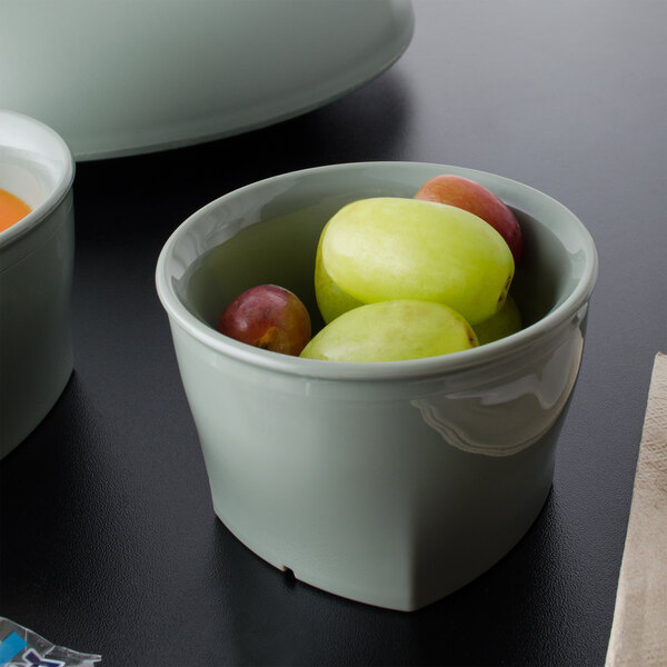 A white Cambro insulated plastic bowl filled with green grapes on a black surface with a white stripe.