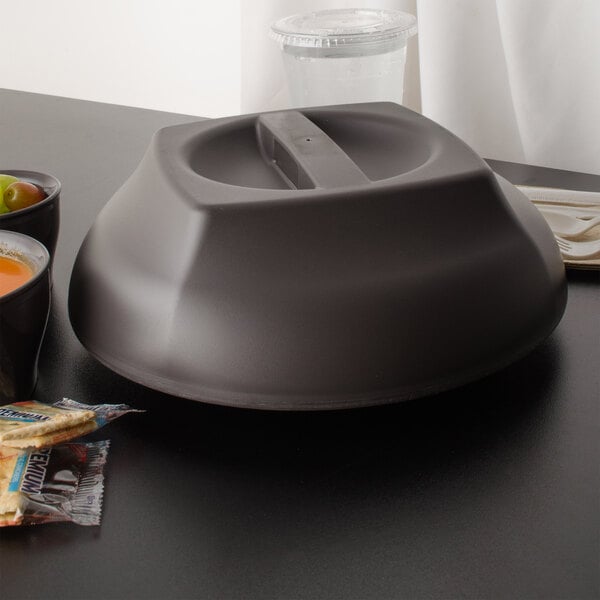 A smoked metal Cambro plate cover on a table with a bowl of fruit.