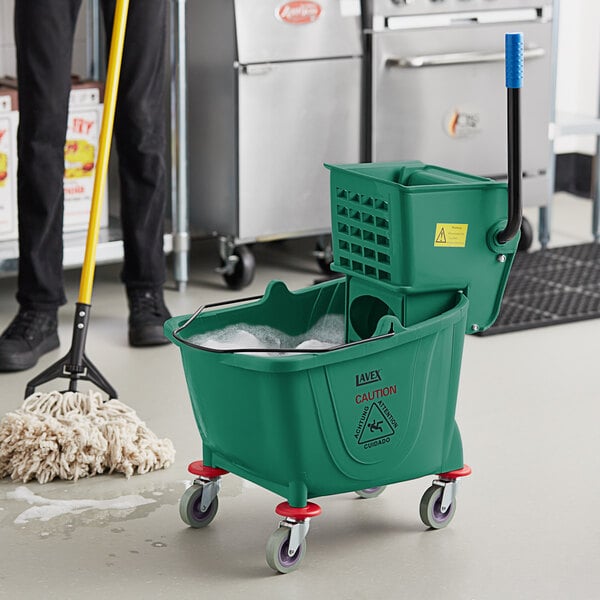 A man using a green Lavex mop and bucket to clean a floor.