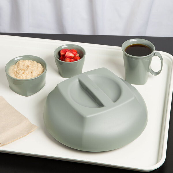 A grey plastic bowl filled with oatmeal and strawberries on a table with a cup of coffee on a tray.