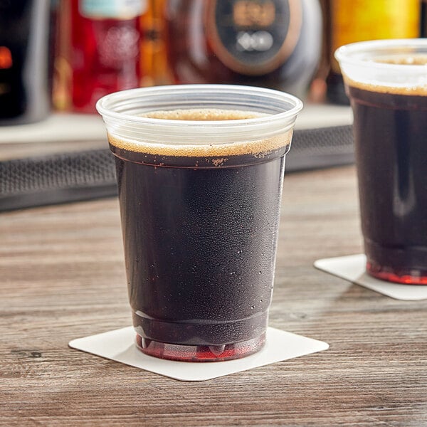 A plastic cup of dark liquid on a table in a bar.