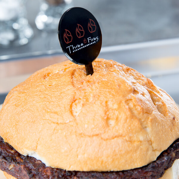 A hamburger with a black oval pick in it.