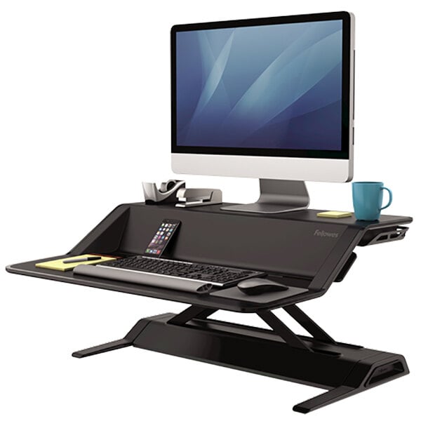 A black and silver Fellowes Lotus sit-stand workstation with a computer, keyboard, and cell phone.