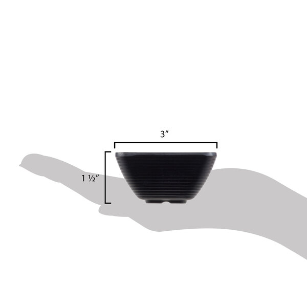 A hand holding a black Tablecraft square ribbed melamine ramekin.
