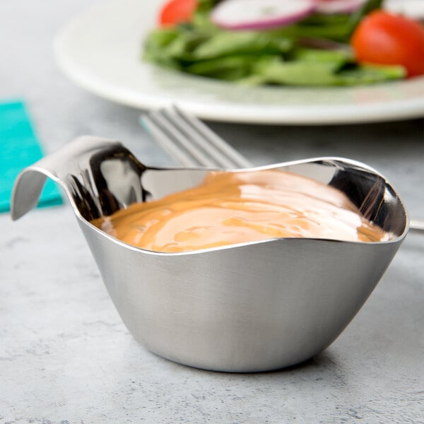 A Tablecraft stainless steel gravy boat filled with sauce on a table.