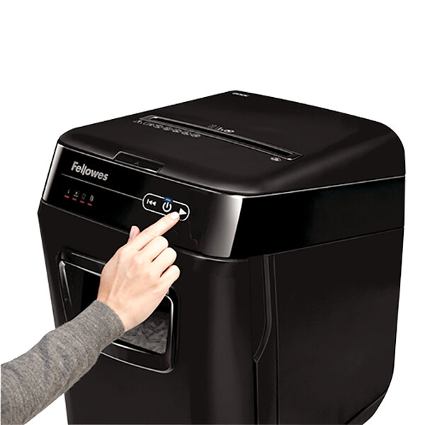 A hand pressing a button on a black Fellowes AutoMax 200C shredder.