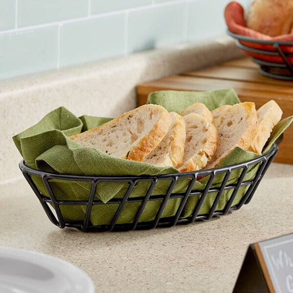 A black Clipper Mill oval wire grid basket filled with sliced bread on a counter.
