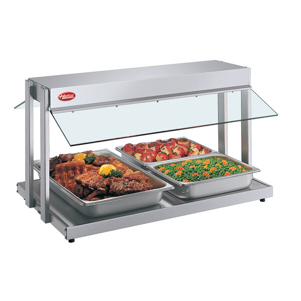 A Hatco countertop buffet warmer with trays of meat and vegetables under a glass cover.