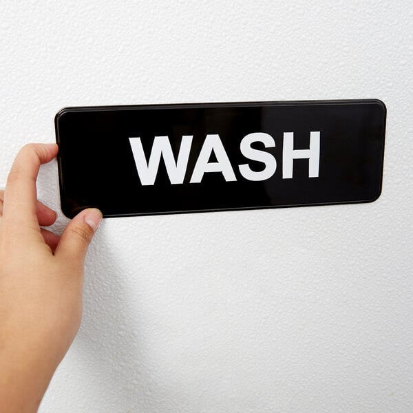 A person's hand holding a black and white Vollrath Traex wash sign.