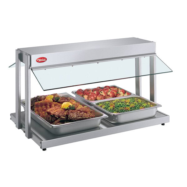 A Hatco glass countertop buffet warmer with trays of meat and vegetables on a counter.