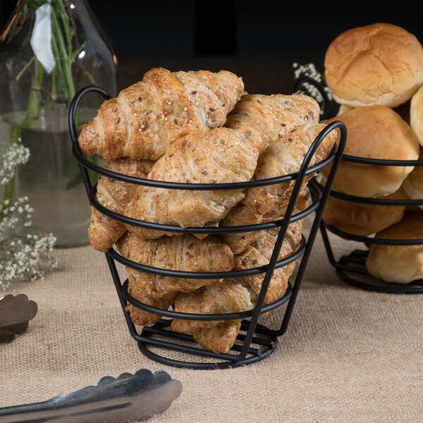 A black Clipper Mill wire basket filled with croissants and rolls.