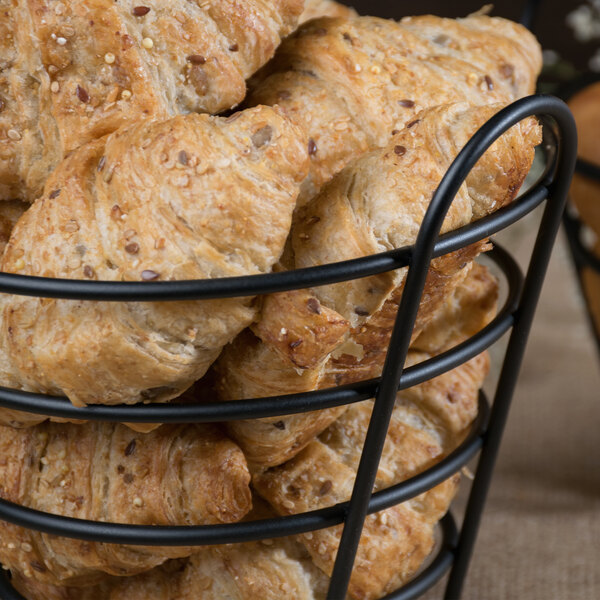 A Clipper Mill black wire round basket filled with croissants.