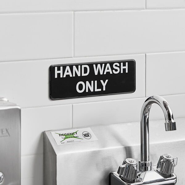 A black and white Vollrath Traex hand wash only sign on a white wall.