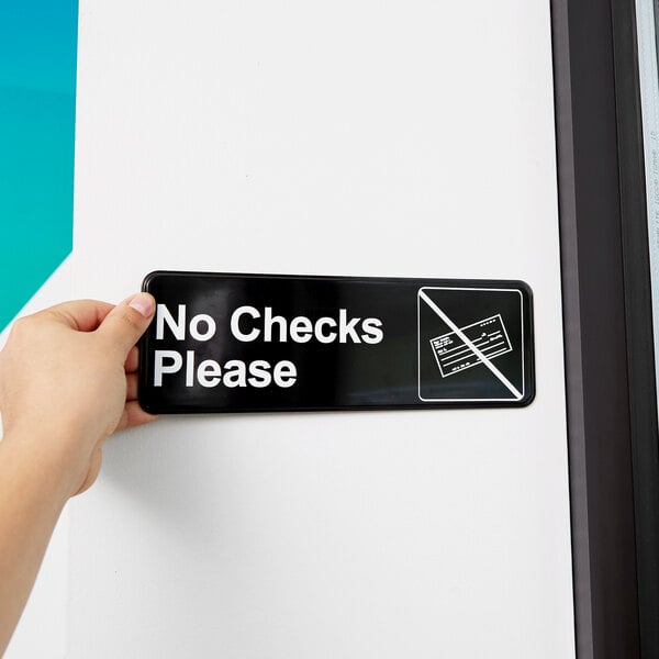 A person holding a black and white Vollrath Traex No Checks Please sign.