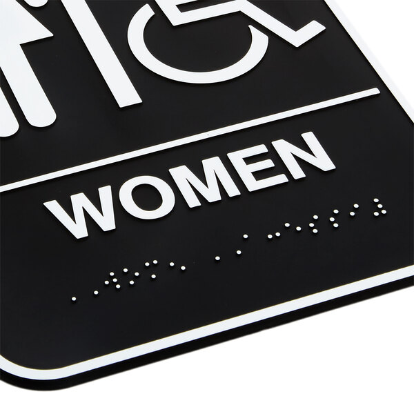 A black and white Vollrath restroom sign with the word "Women" and Braille.