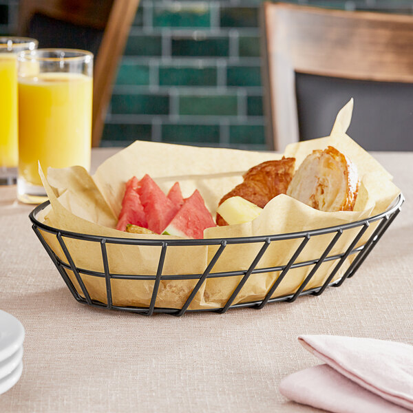 A Clipper Mill black wire grid basket with fruit and bread on a table.